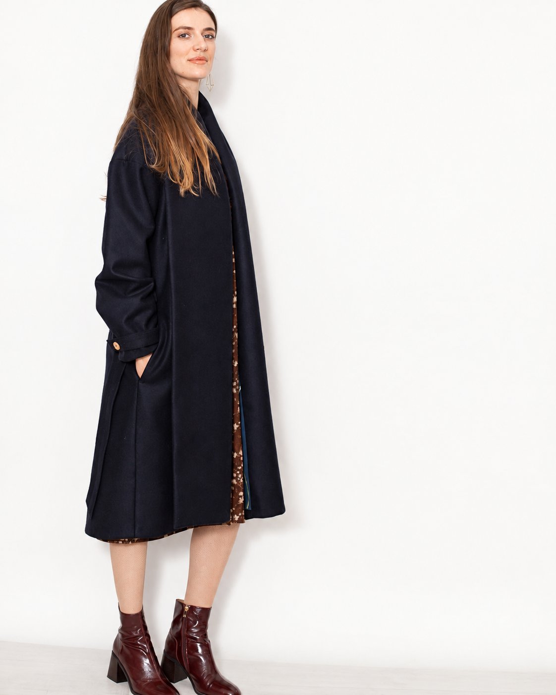 Manteau Aglaé marine en laine vierge porté ouvert de trois quarts avec une robe imprimée et des bottines.